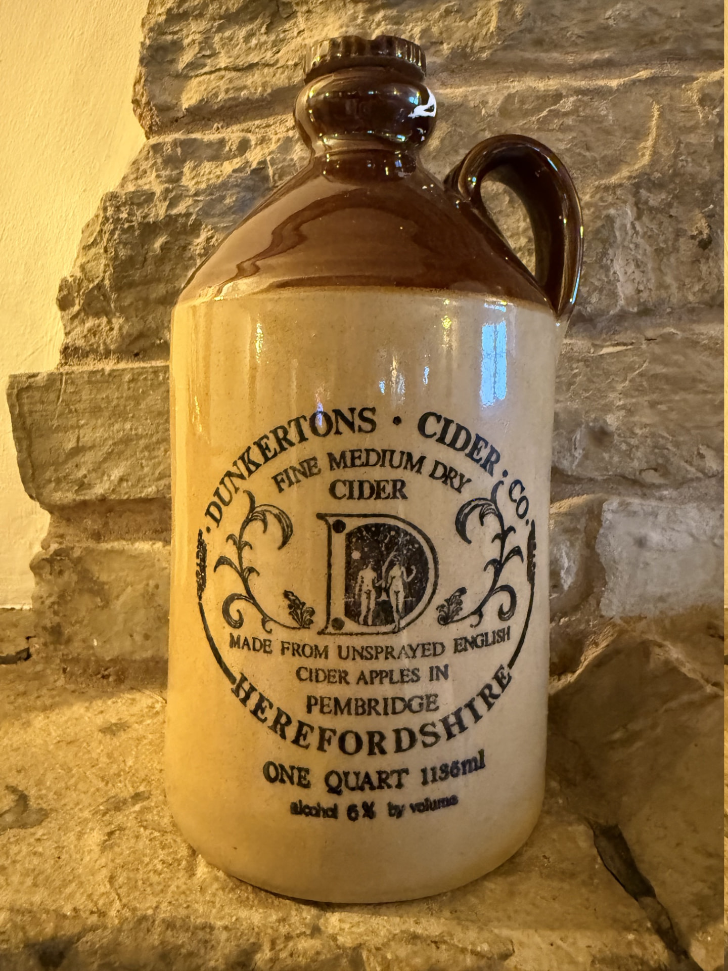 A Dunkertons Herefordshire cider stoneware flagon on the stone hearth