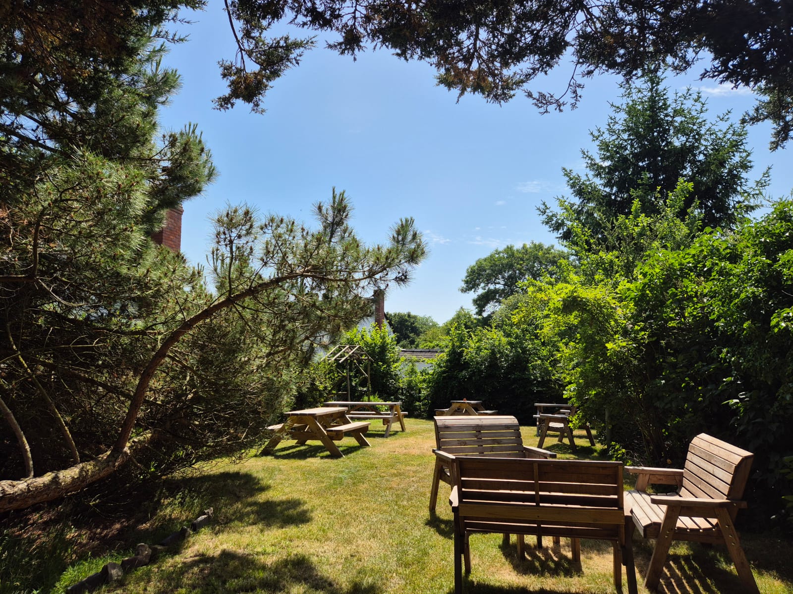 Sunlit lawn with picnic tables and benches in the garden at The Bell Inn